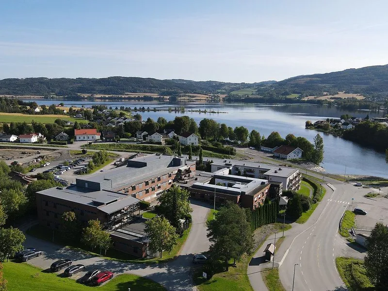 Bildet er et dronefoto som viser Jevnaker omsorgs- og rehabiliteringssenter med Randsfjorden i bakgrunnen.