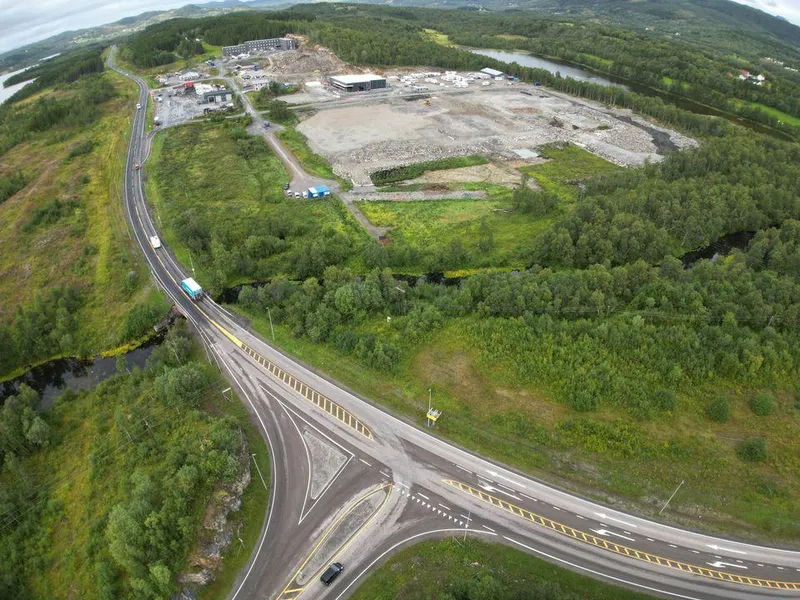 Bildet er et dronebilde av dagens kryssløsning på E10 ved Harstad/Narvik lufthavn Evenes. Bildeteksten sier, Dronebilde av dagens kryss og avkjøring fra E10 til Harstad/Narvik lufthavn Evenes. På avbildet strekning er fartsgrensen satt ned til 50 km/t for å redusere faren for trafikkulykker, frem til nytt og trafikksikkert kryss er etablert.