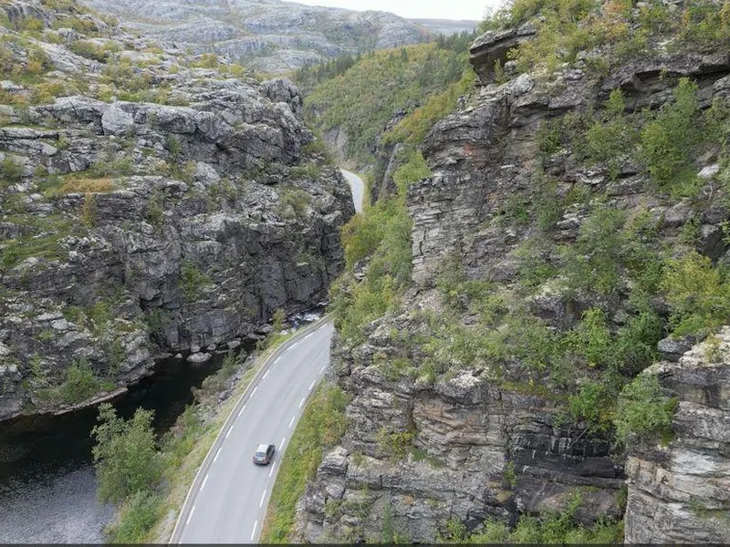 Bildet er et dronebilde som viser E45 dypt nede i en evledal. Bildeteksten sier: Flaskehalsen: Dagens E45 gjennom kløfta følger en naturlig elvecanyon. Den skjærer seg dypt ned i fjellet fra Finnmarksvidda mot Alta. Fjellet er dårlig og porøst. Snøskred, sørpeskred og steinras gir ofte stengt veg. Nå skal strekningen legges i tunnel.