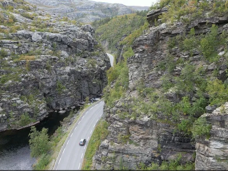 Bildet er et dronebilde av E45 der vegen slynger seg langs Eibyelva igjennom  en canyon med stupbratte fjell på begge sider. Bildeteksten sier, Flaskehalsen: Dagens vei gjennom kløfta følger en naturlig elvecanyon som skjærer seg ned igjennom fjellet fra Finnmarksvidda mot Alta. Fjellet har dårlig kvalitet og det går ofte snøskred, sørpeskred og steinras på strekningen.
