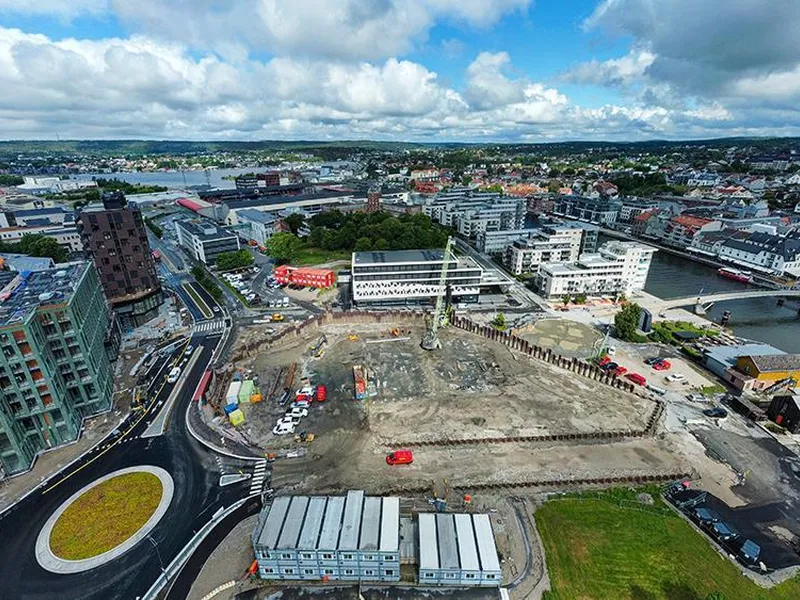 Dronebilde over tomt med bygg, blokker, brakker og elv rundt - Klikk for stort bilde