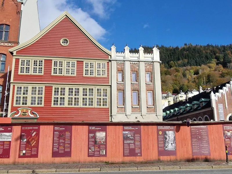 Bildet viser fasaden på Finnegården, Bryggen i Bergen, som består av en rød trebygning (Sjøstuen) og Murtasken. Foran fasaden er et byggegjerde.