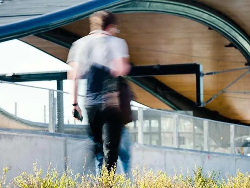 Mann går mot togstasjonen. Stasjonstaket er buet i bakgrunnen og i forgrunnen er det trær.