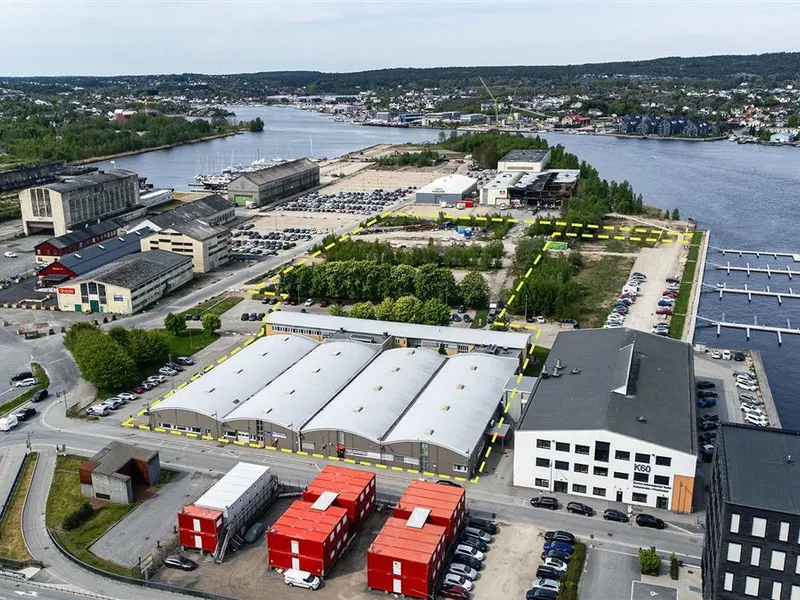 Dronebilde av tomt med bygg, trær og vann på sidene - Klikk for stort bilde